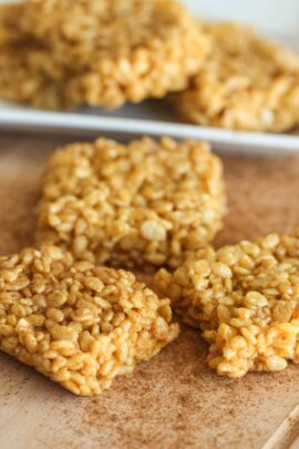 Close-up of four cereal bar squares on a wooden surface, with a few more cereal bars blurred in the background.