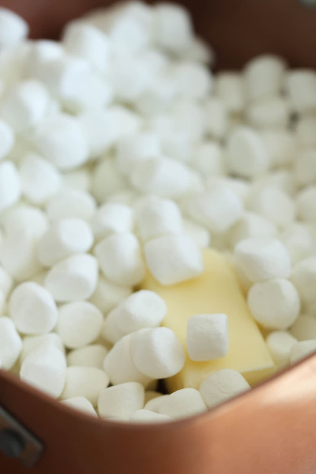 A metal bowl filled with mini marshmallows and a piece of butter.