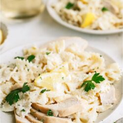 Two plates of pasta topped with sliced chicken and small sliced lemon wedges.