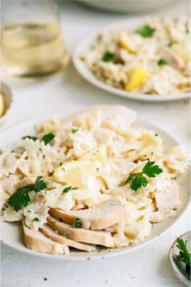 Two plates of pasta topped with sliced chicken and small sliced lemon wedges.