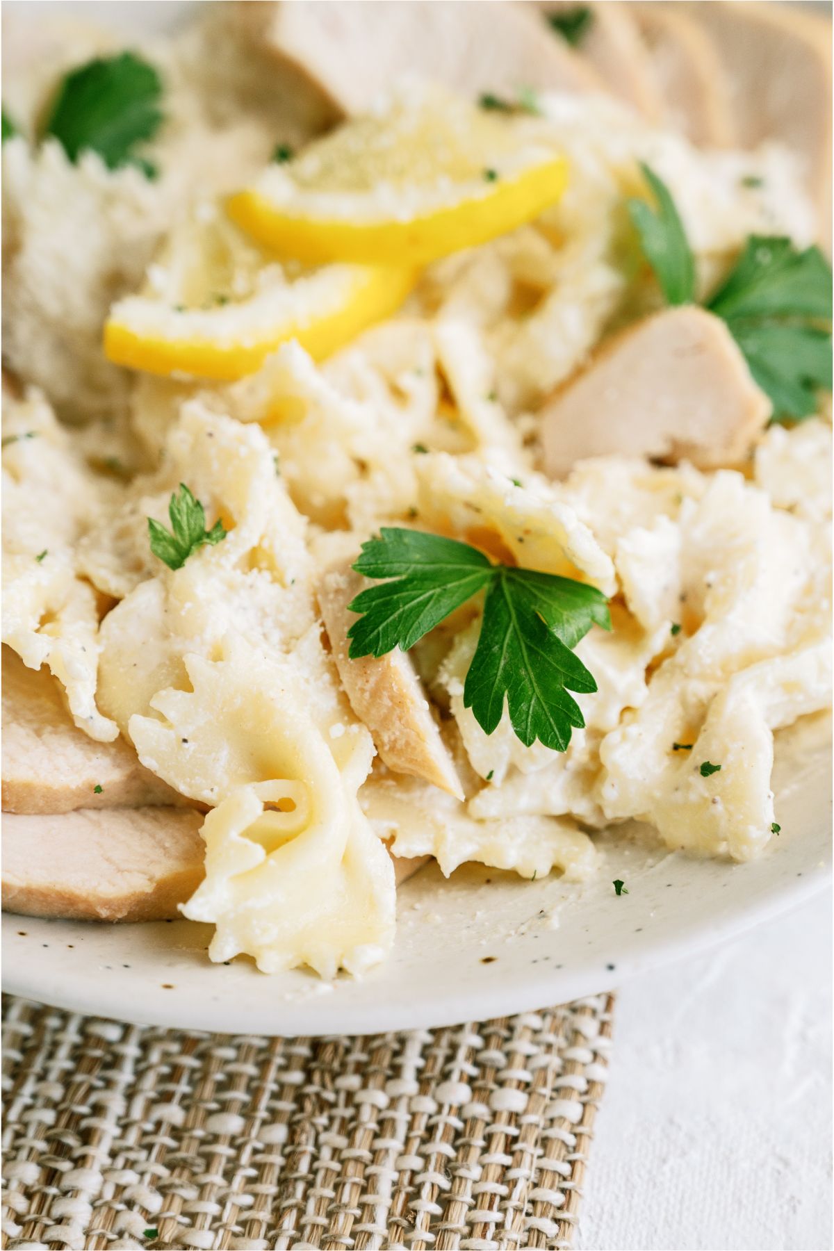 A plate with bowtie pasta, sliced chicken and sliced limes. Topped with fresh parsley and shredded cheese. 