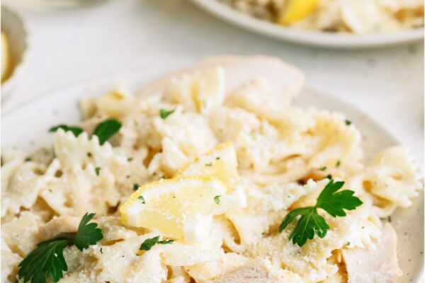 Two plates of pasta topped with sliced chicken and small sliced lemon wedges.