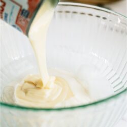 Pouring condensed milk into a glass bowl filled with cold water.