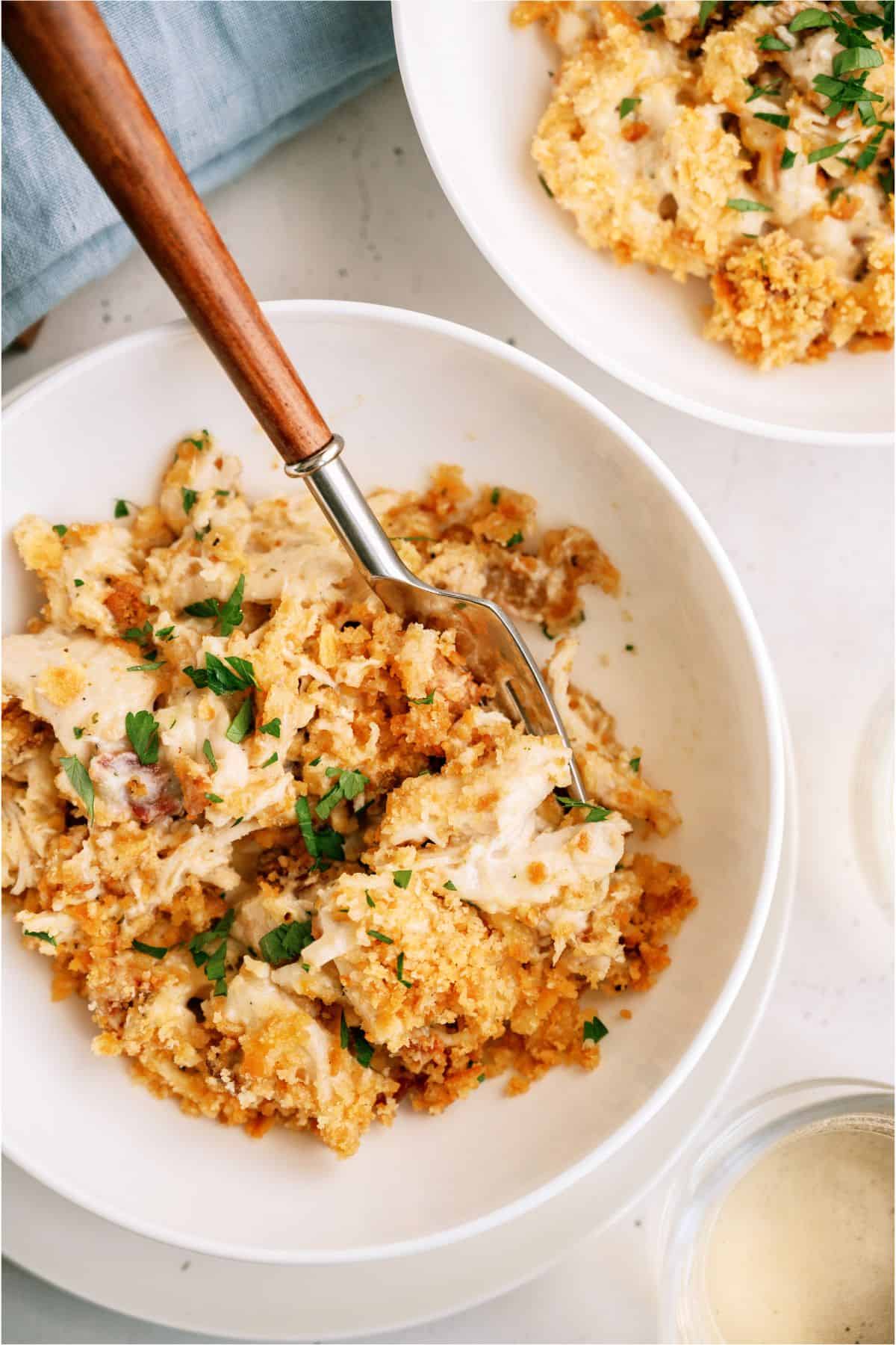 A bowl of cracked chicken casserole topped with fresh parsley and breadcrumbs, with a fork placed in the bowl. Another dish with the same meal is partially visible next to it.