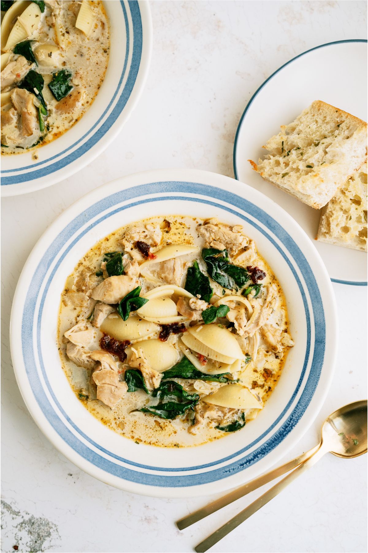 Top view of a bowl of chicken soup with a small plate of garlic bread and another bowl of soup in the background.