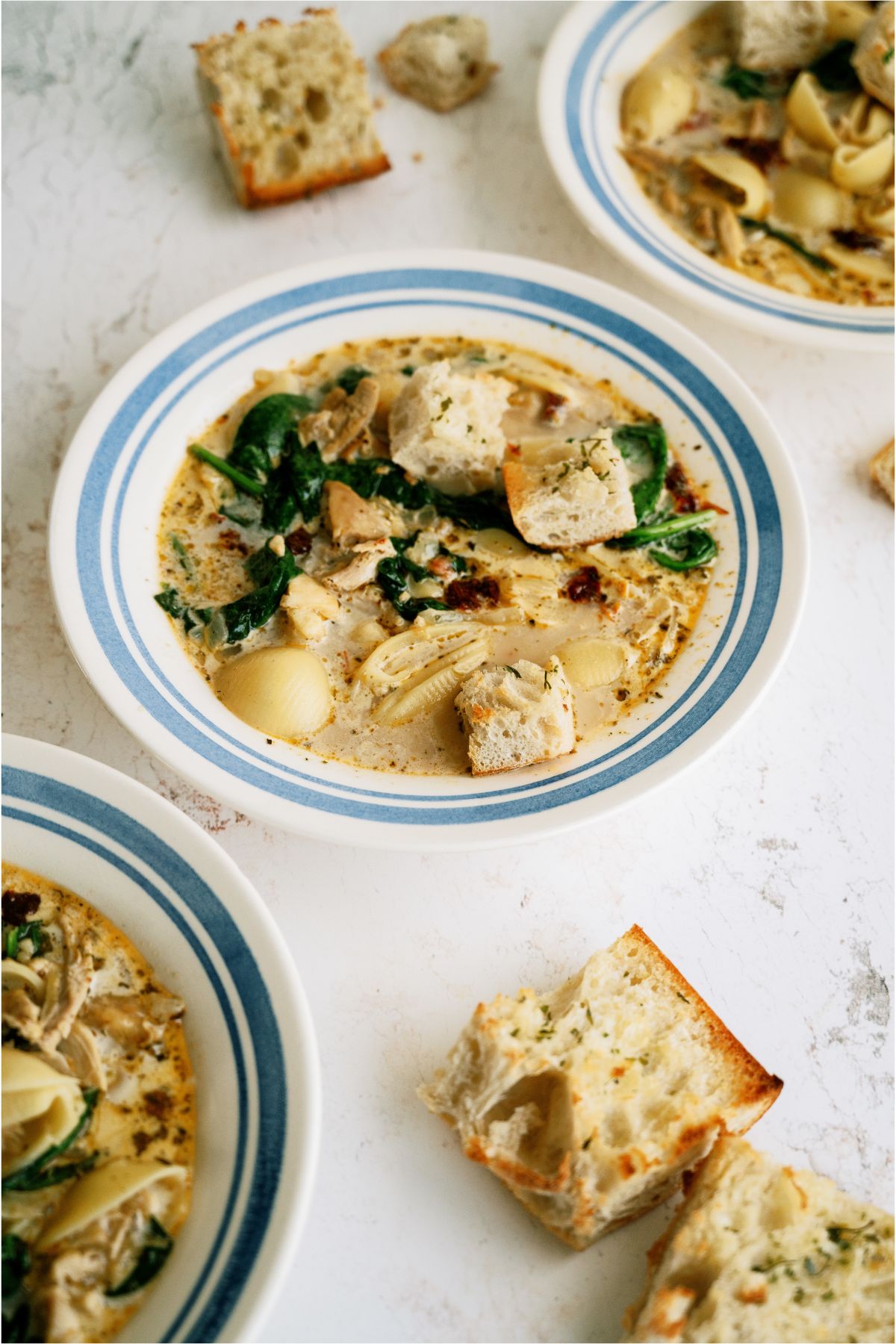 3 bowls of Marry Me Chicken Soup with one centered surround by pieces of garlic bread.