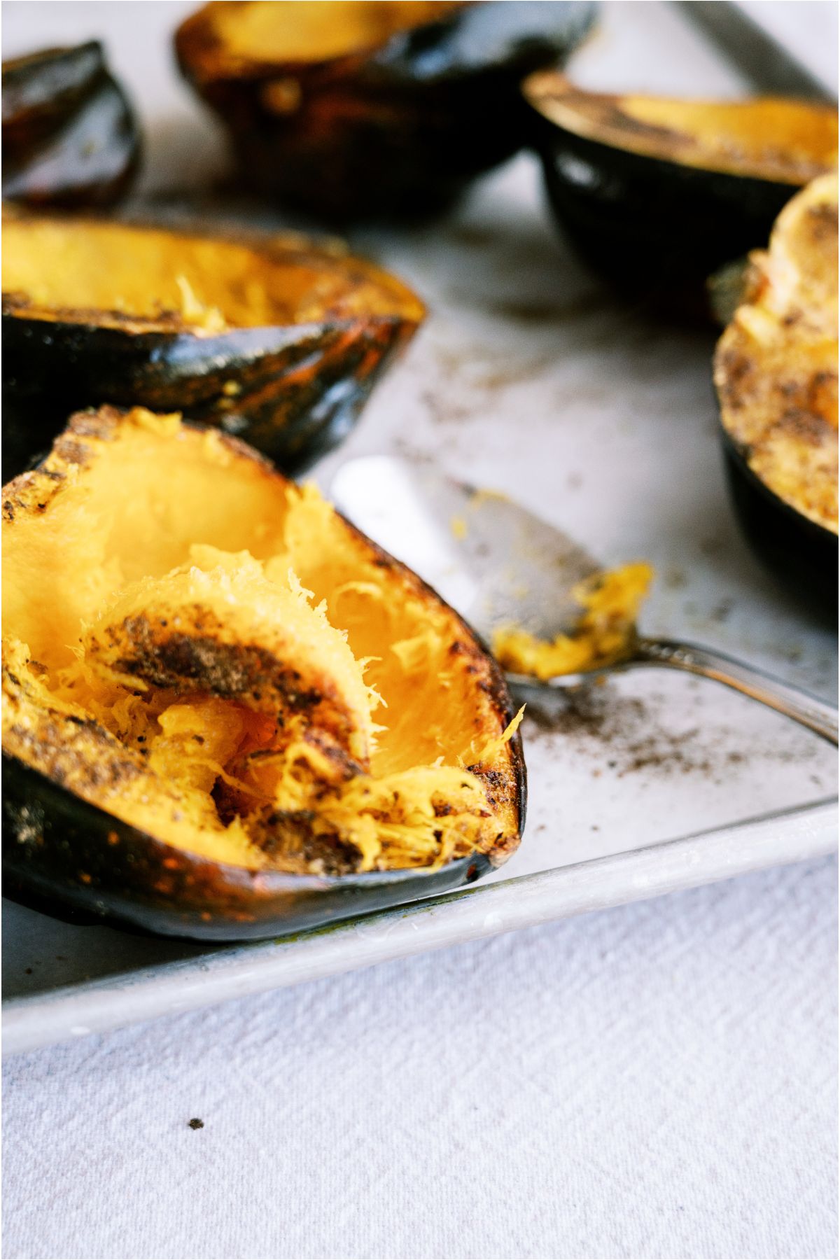 Roasted Acorn Squash on a baking sheet with a spoon loosening the insides of the squash.