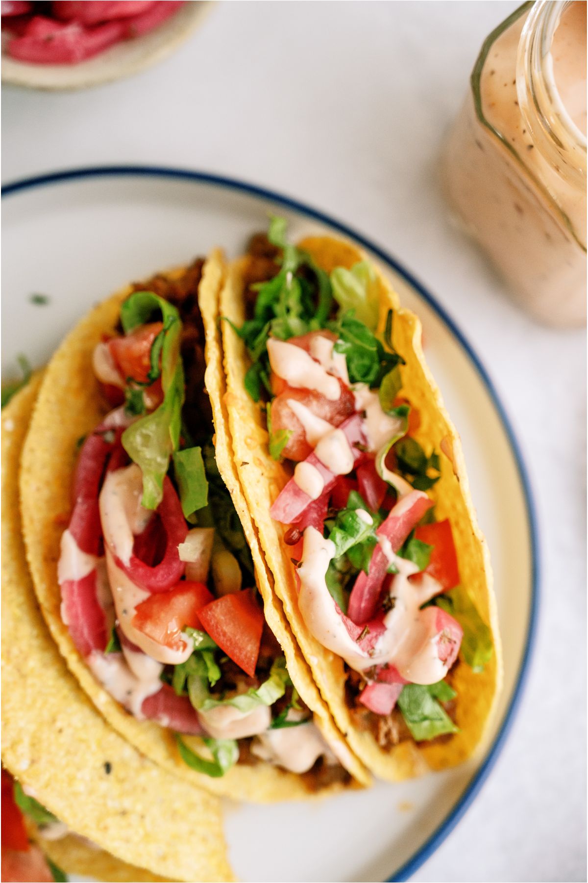 Top view of Cheeseburger Tacos on a plate with toppings and sauce.