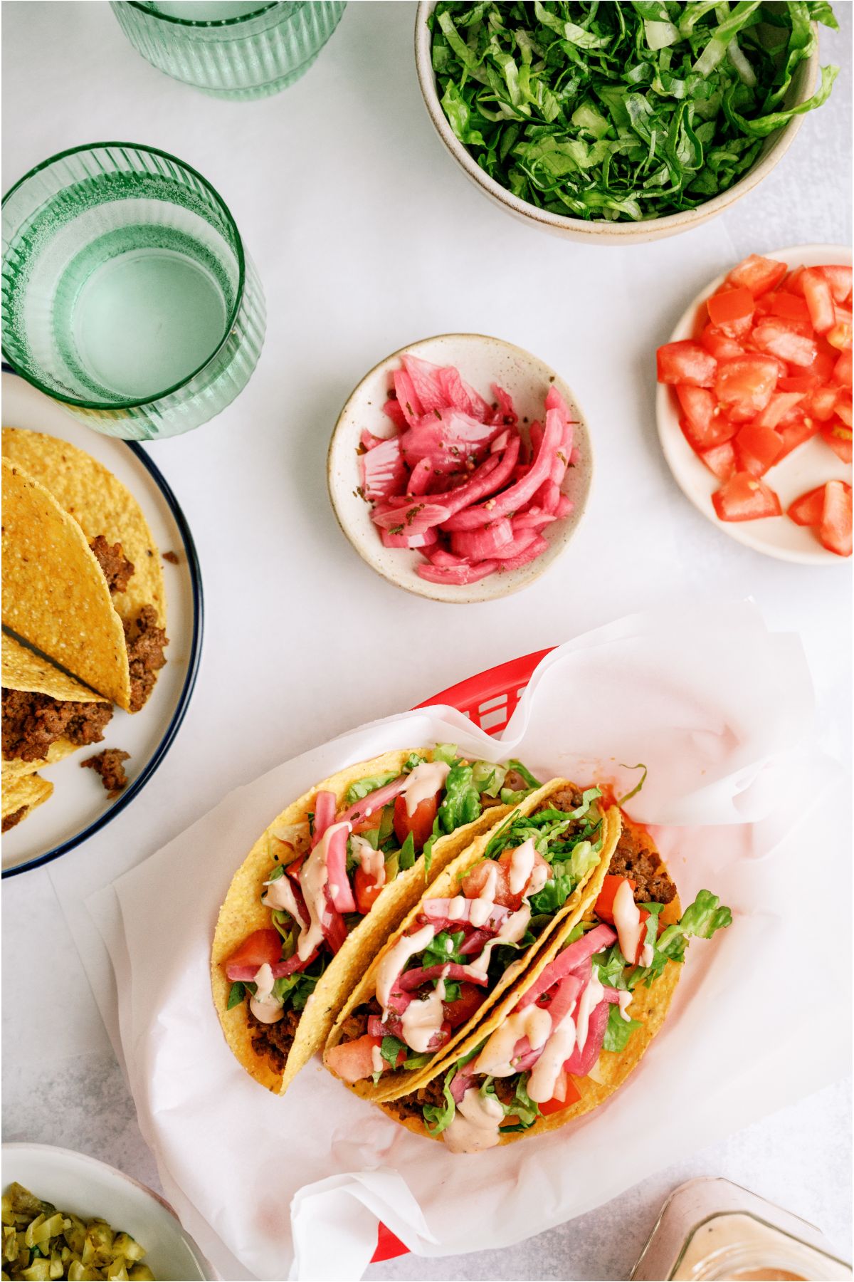 Top view of Cheeseburger Tacos in a basket lined with parchment paper. Surrounded by bowls of toppings.