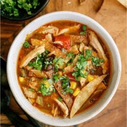 Top view of a bowl of Easy Crock Pot Chicken Tortilla Soup topped with fresh cilantro, with a bowl of additional chopped cilantro in the background.