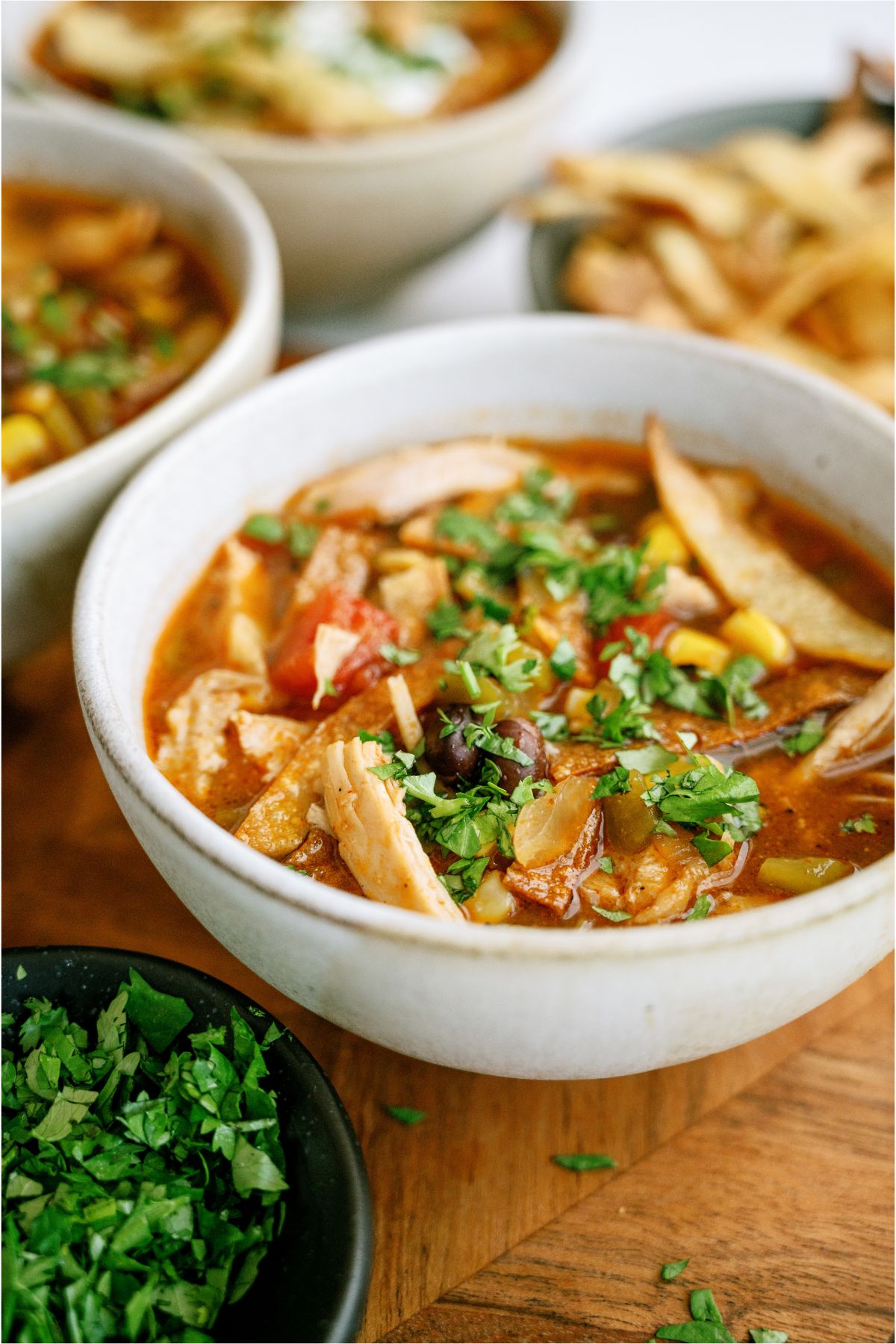 A white bowl of Easy Crock Pot Chicken Tortilla Soup topped with tortilla strips and cilantro. Several other bowls of soup in the background.