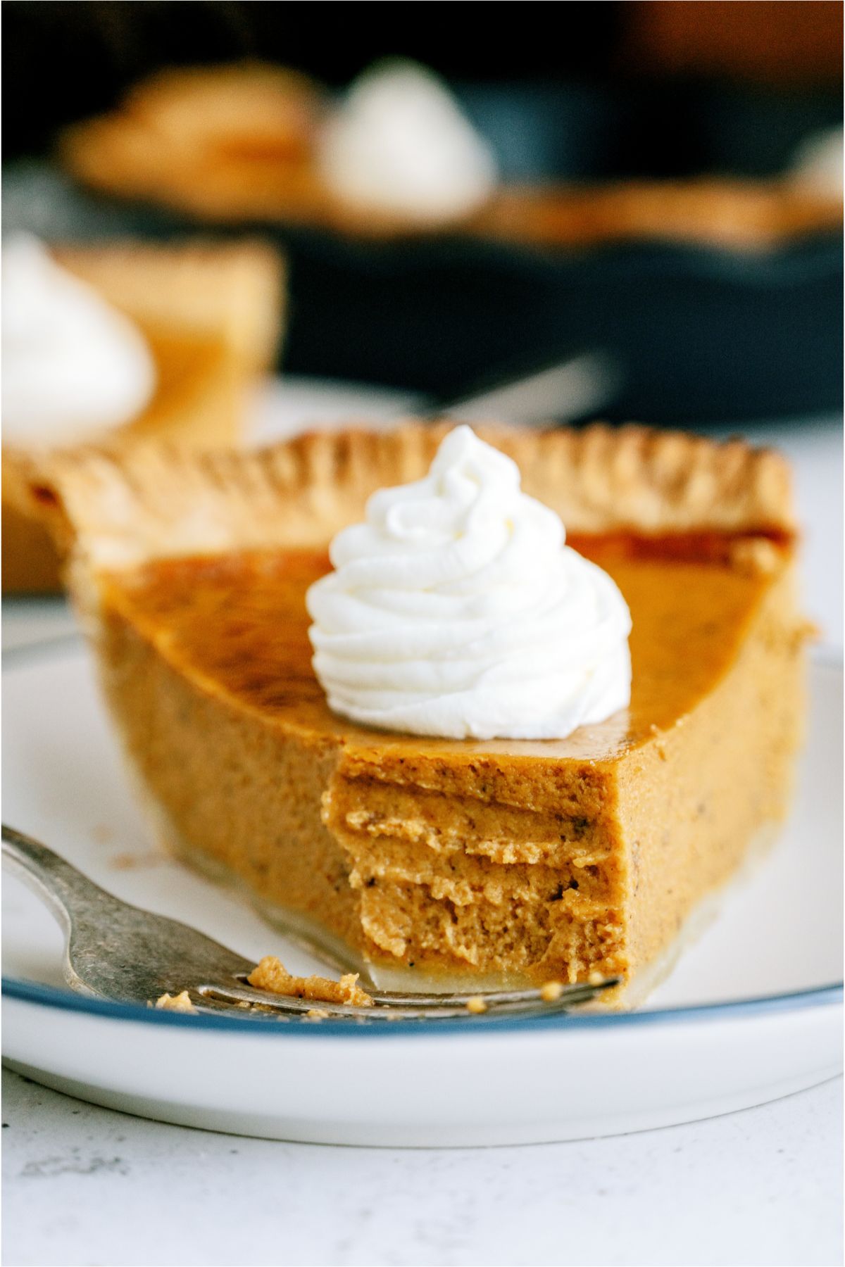 A slice of pumpkin pie with a bite missing on a plate with a fork.