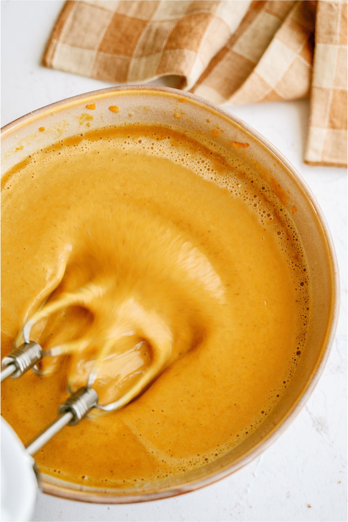 Hand mixer beating pumpkin pie filling in mixing bowl.