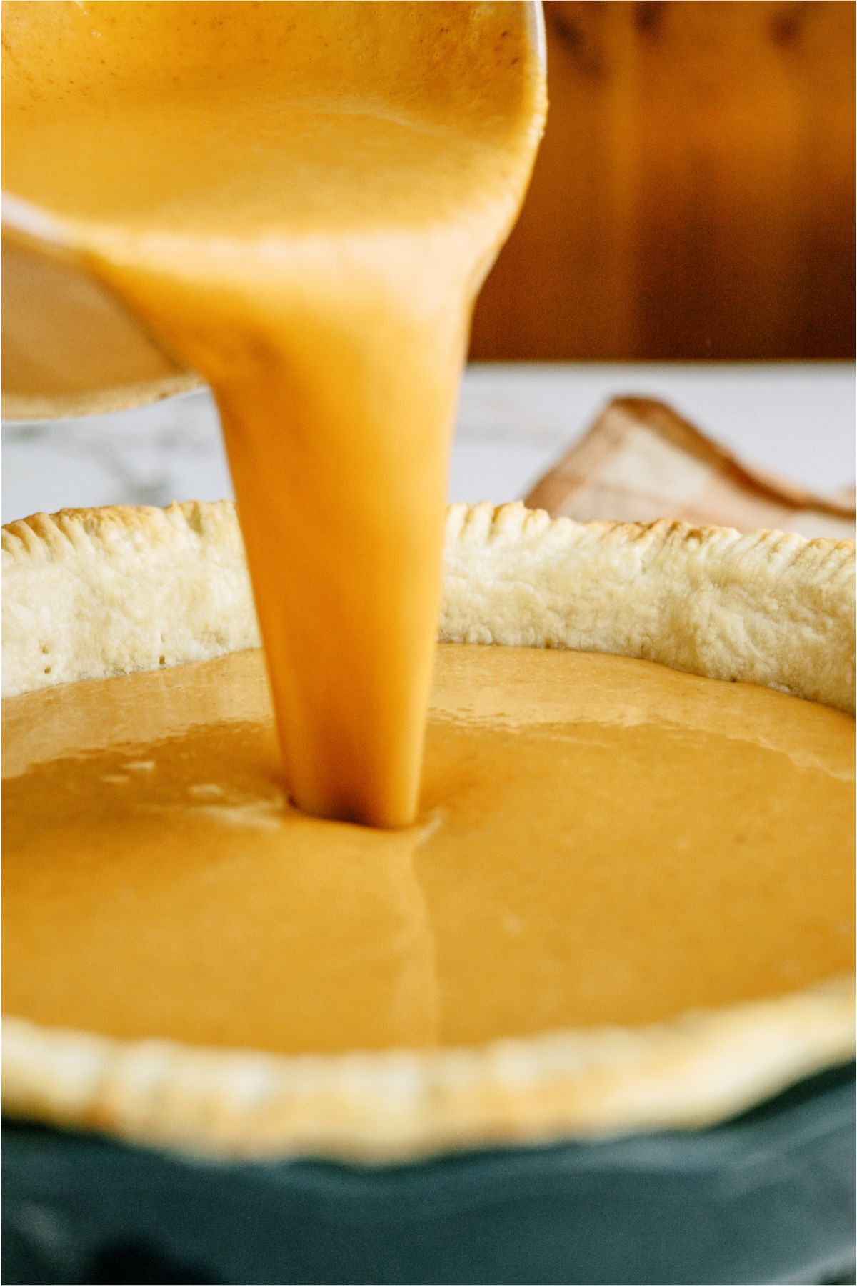 Pouring homemade pumpkin pie filling from mixing bowl into baked pie crust.