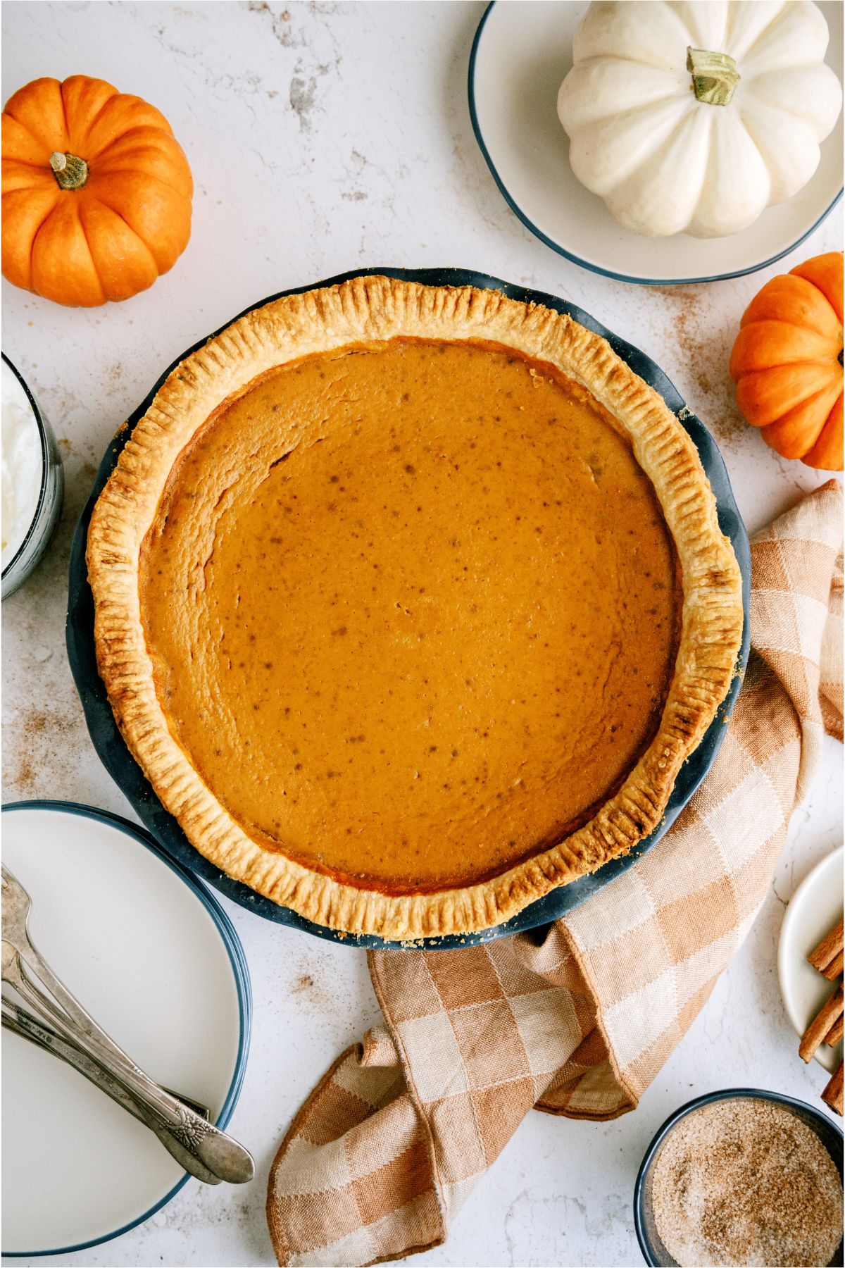 Baked Homemade Fresh Pumpkin Pie surrounded by little pumpkins and a hand towel. 