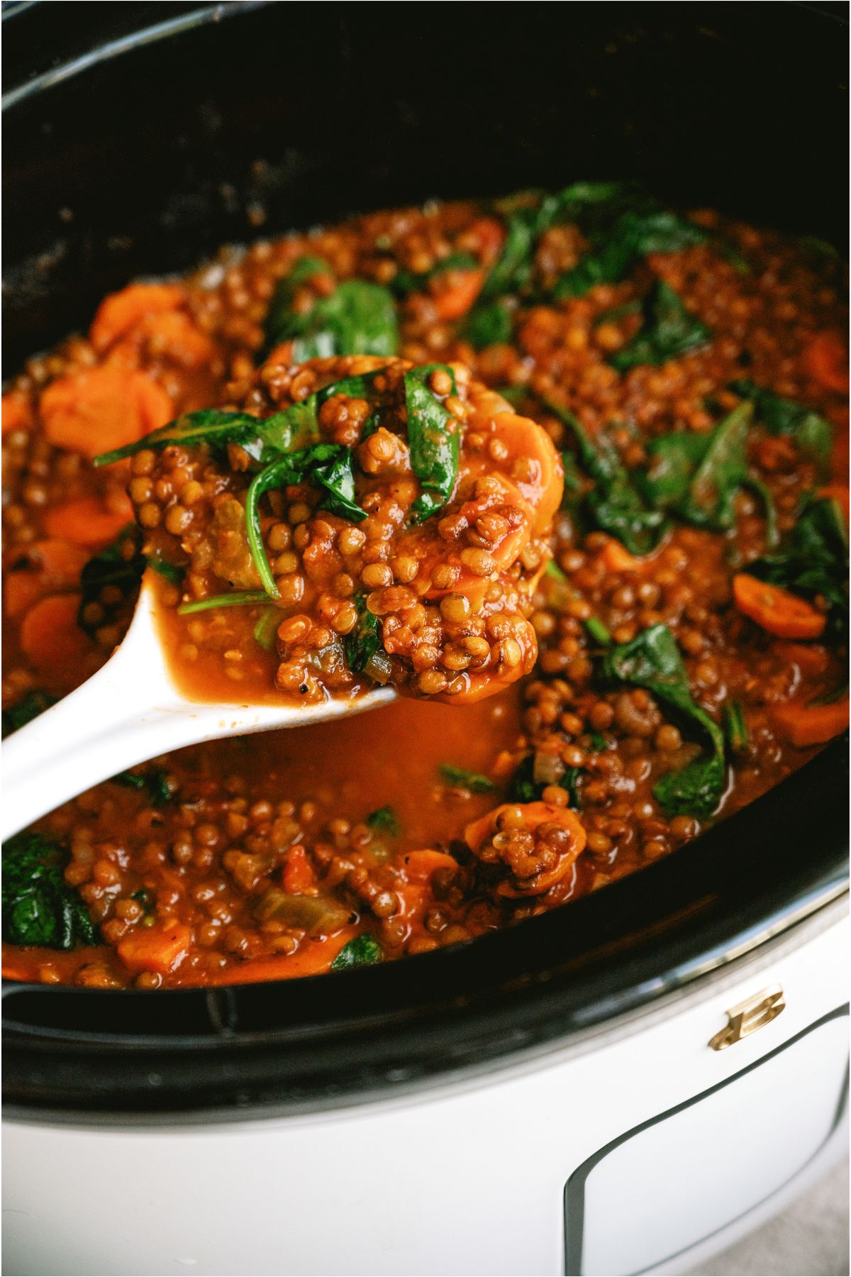 A serving spoon lifting a scoop of Slow Cooker Lentil Soup out of the Slow Cooker.