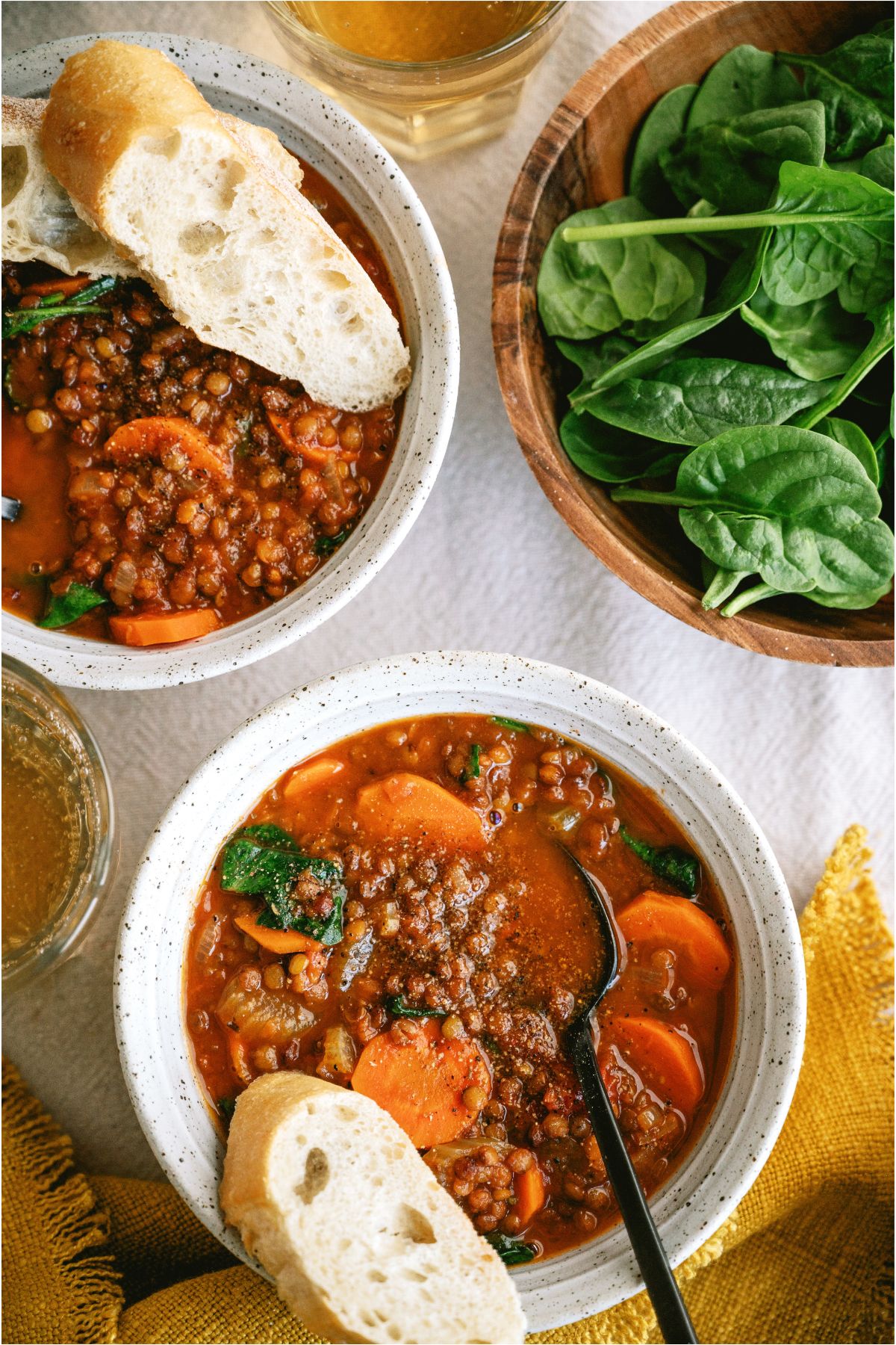 Top view of 2 bowls of Slow Cooker Lentil Soup with bread in each bowl. A small bowl of fresh spinach on the side.