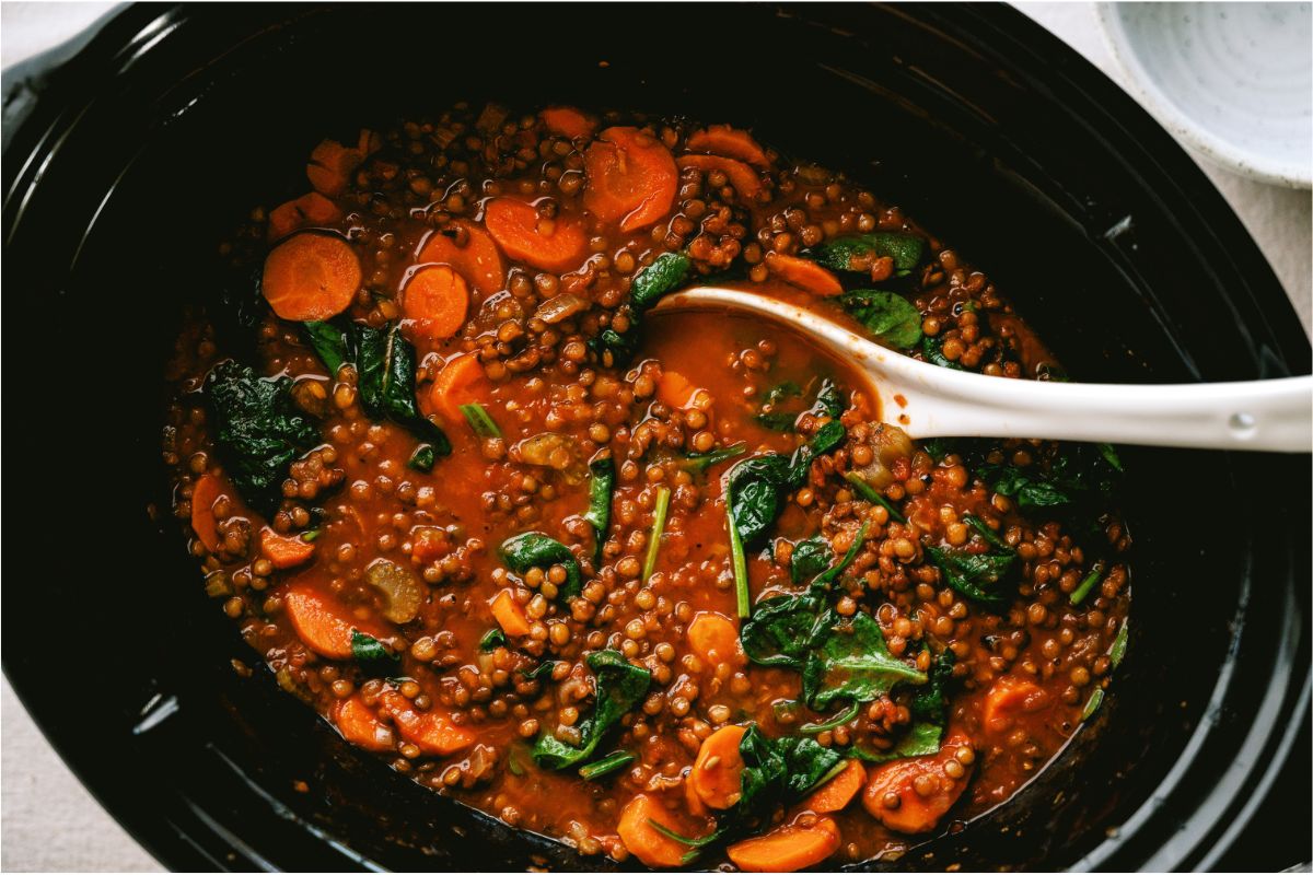 A slow cooker filled with Slow Cooker Lentil Soup and a serving spoon.