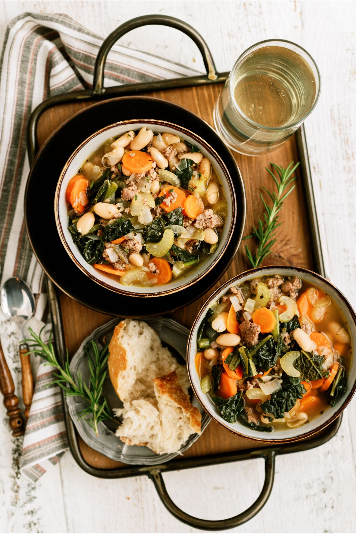 2 bowls of Tuscan White Bean Soup on a serving tray with a glass of water and a side of bread.