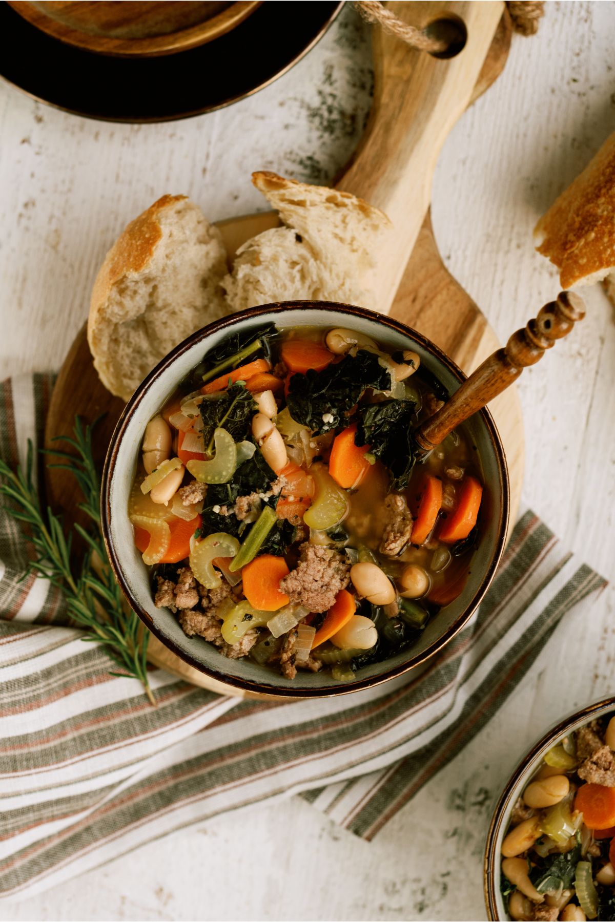 Top view of a bowl of Tuscan White Bean Soup with a spoon. Bread on the side.