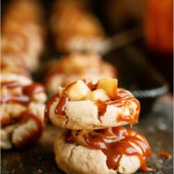 Two Apple Pie Cookies with drizzled caramel stacked on top of each other with the other Apple Pie Cookies in the background.