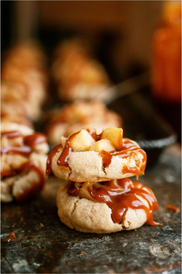 Two Apple Pie Cookies with drizzled caramel stacked on top of each other with the other Apple Pie Cookies in the background.