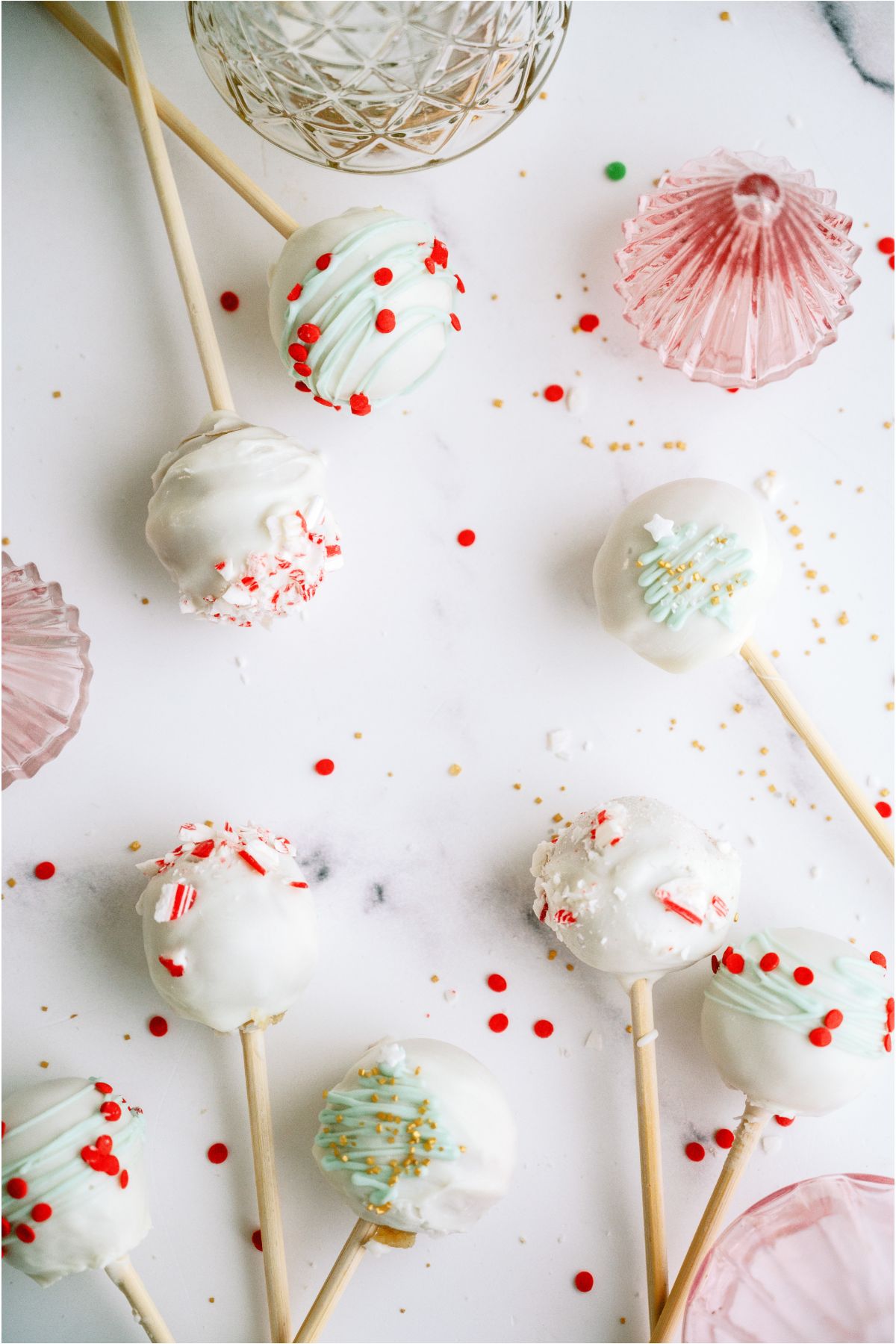 Several Decorated Christmas Cake Pops on a counter with Christmas Decor.