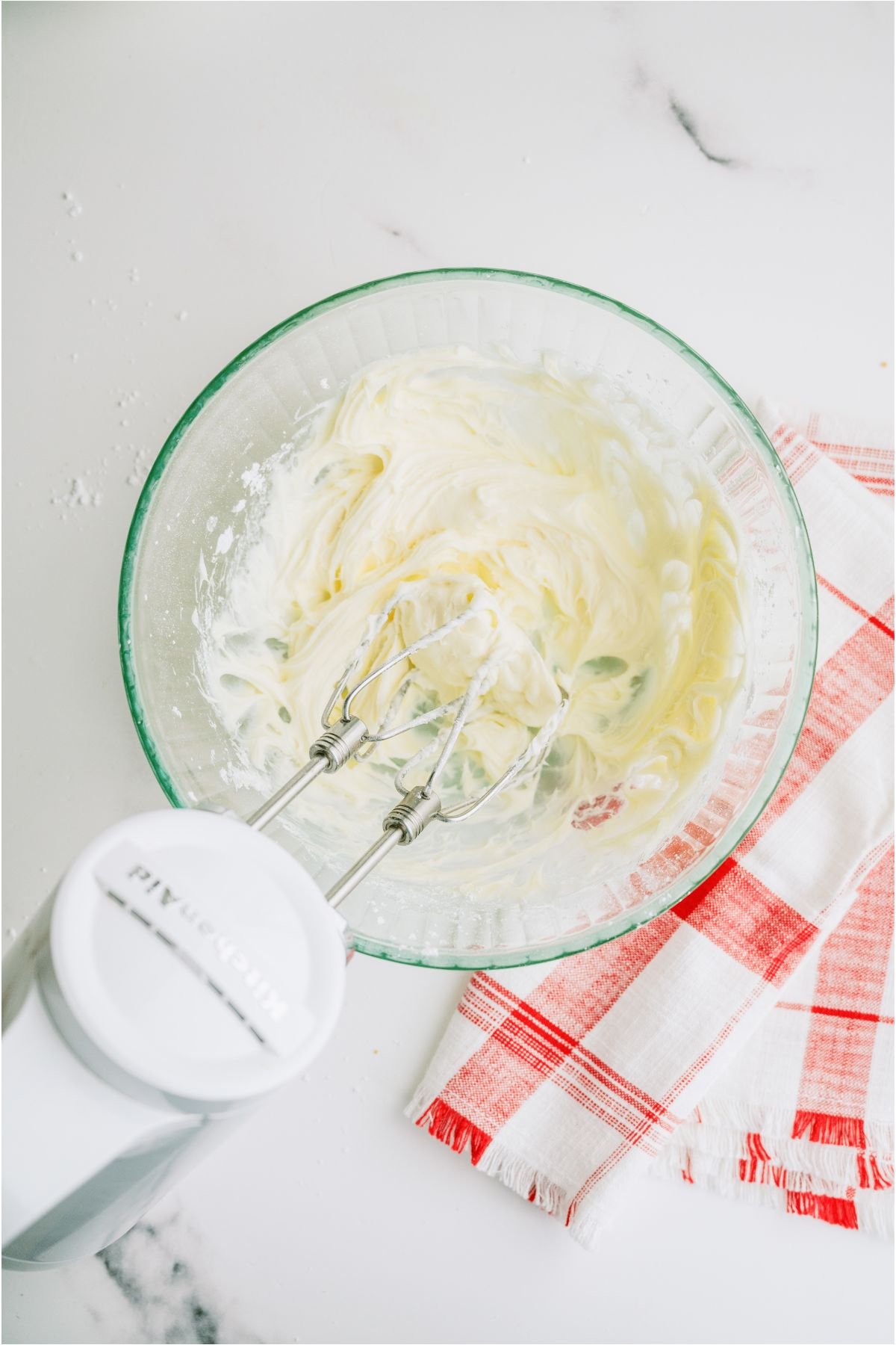 Ingredients for frosting mixed together with a hand mixer in a glass bowl.