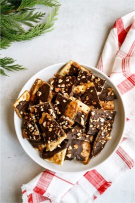 A plate full of broken pieces of Christmas Crack. With a sprig of a pine tree and a Christmas towel underneath the bowl.