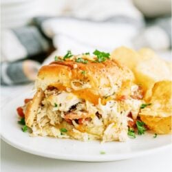 Crack Chicken Slider sandwich on a white plate with chips. Pan of Crack Chicken Sliders in the background.