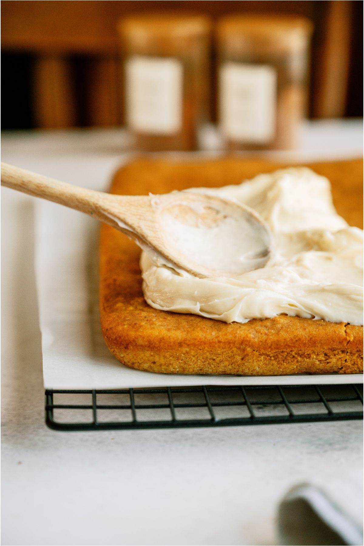 Spreading cream cheese frosting on pumpkin bars with a wooden spoon.