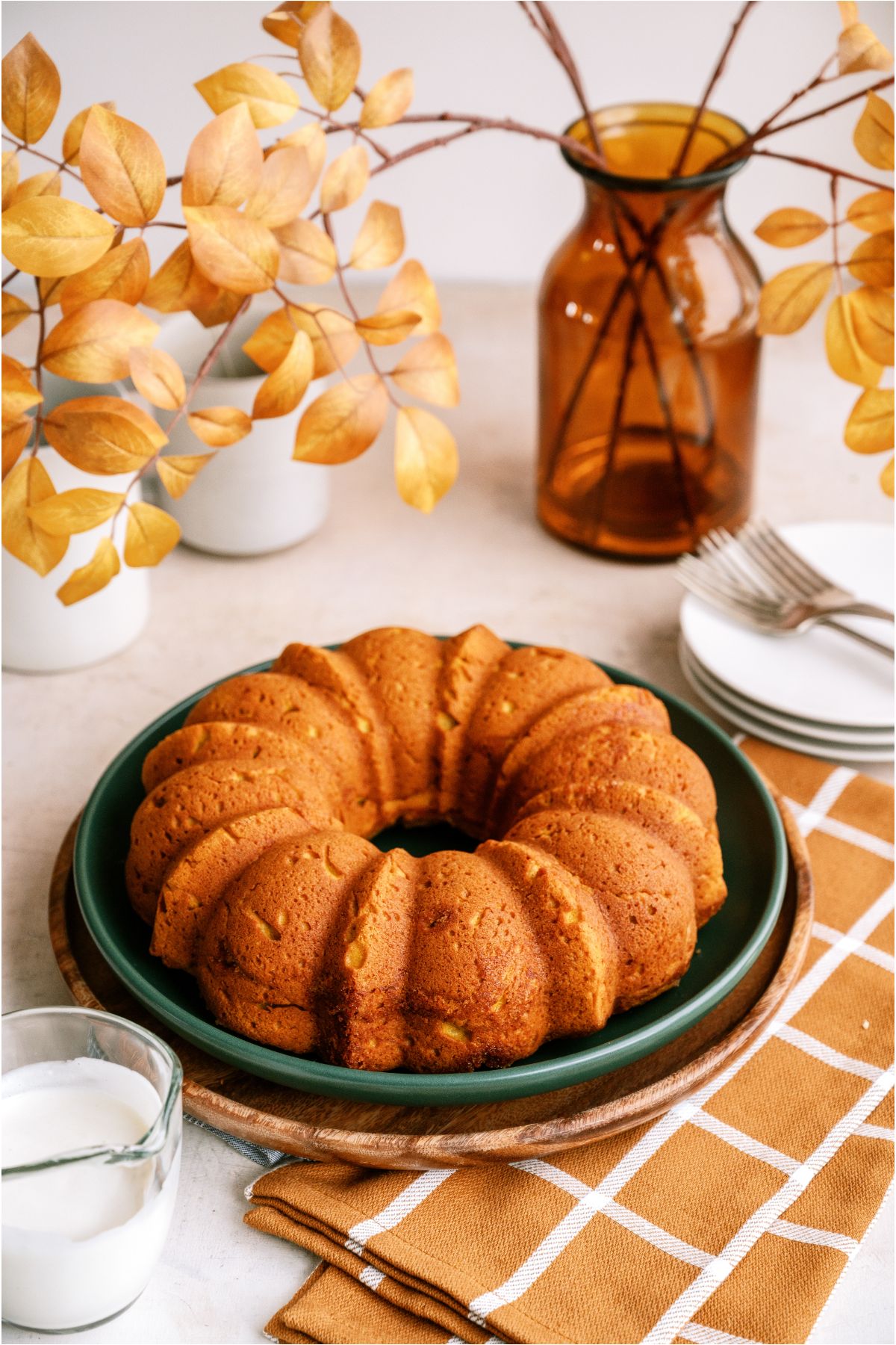 Pumpkin Bundt Cake on a serving plate without the cream cheese glaze. Fall leaves in a vase in the background.