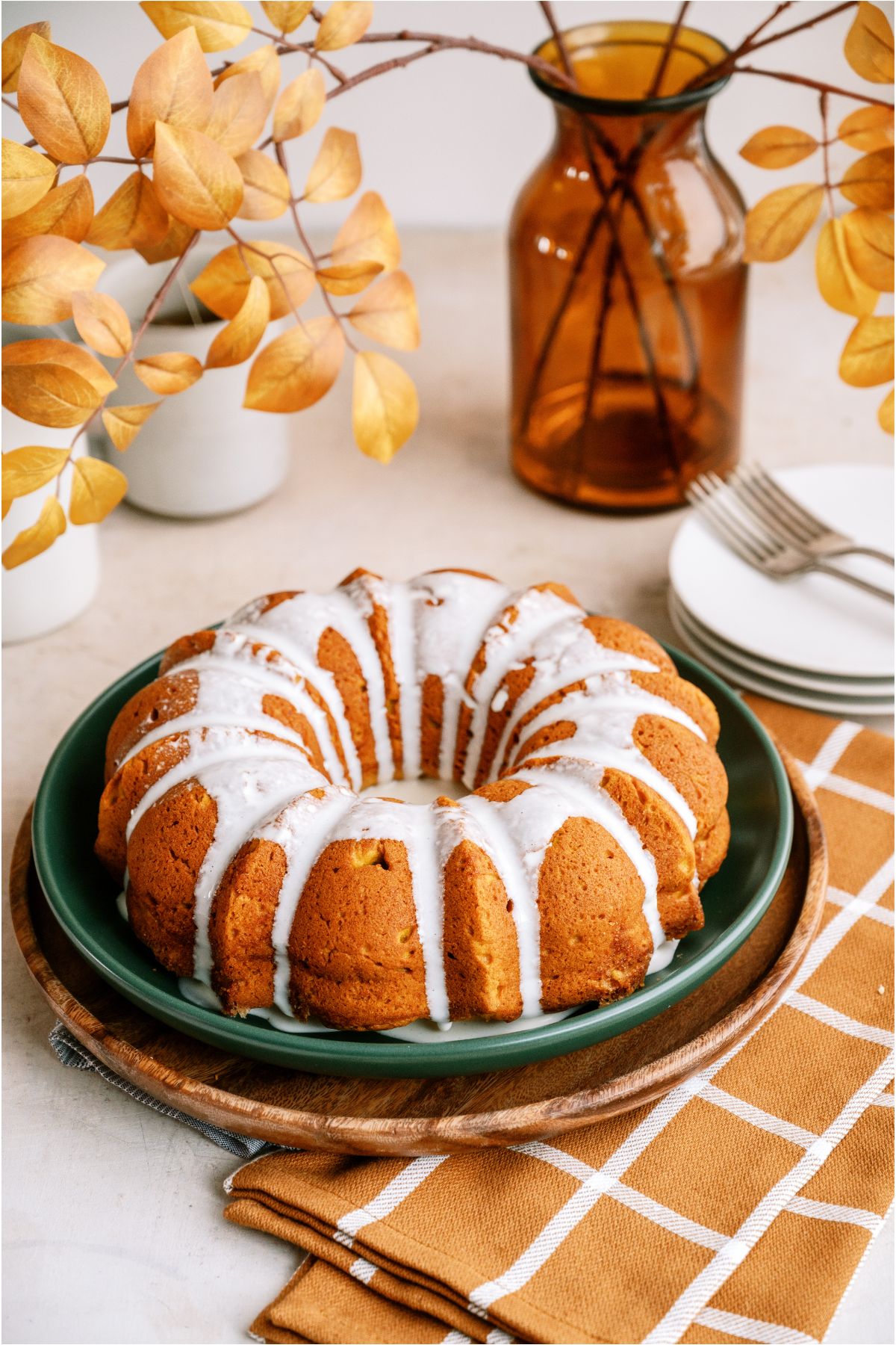 Pumpkin Bundt Cake with cream cheese glaze on a serving plate with a vase of Fall leaves in the background.