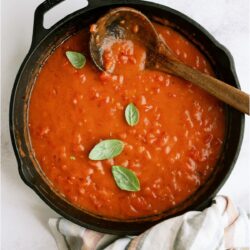 A large skillet on top of a striped towel filled with Tomato Gravy with a wooden spoon.