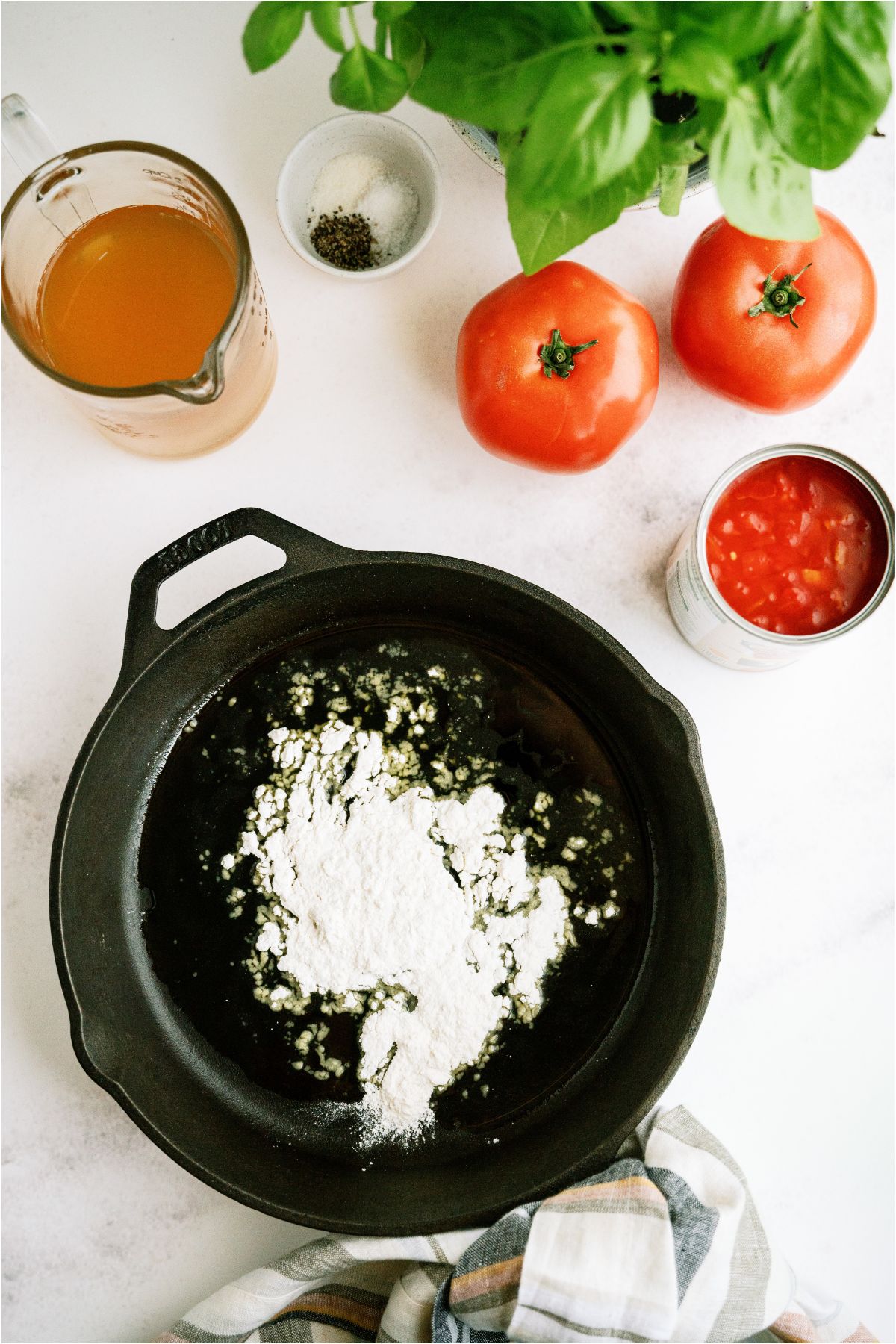 Large skillet with flour sprinkled in the bottom. With fresh and canned tomatoes in the background.