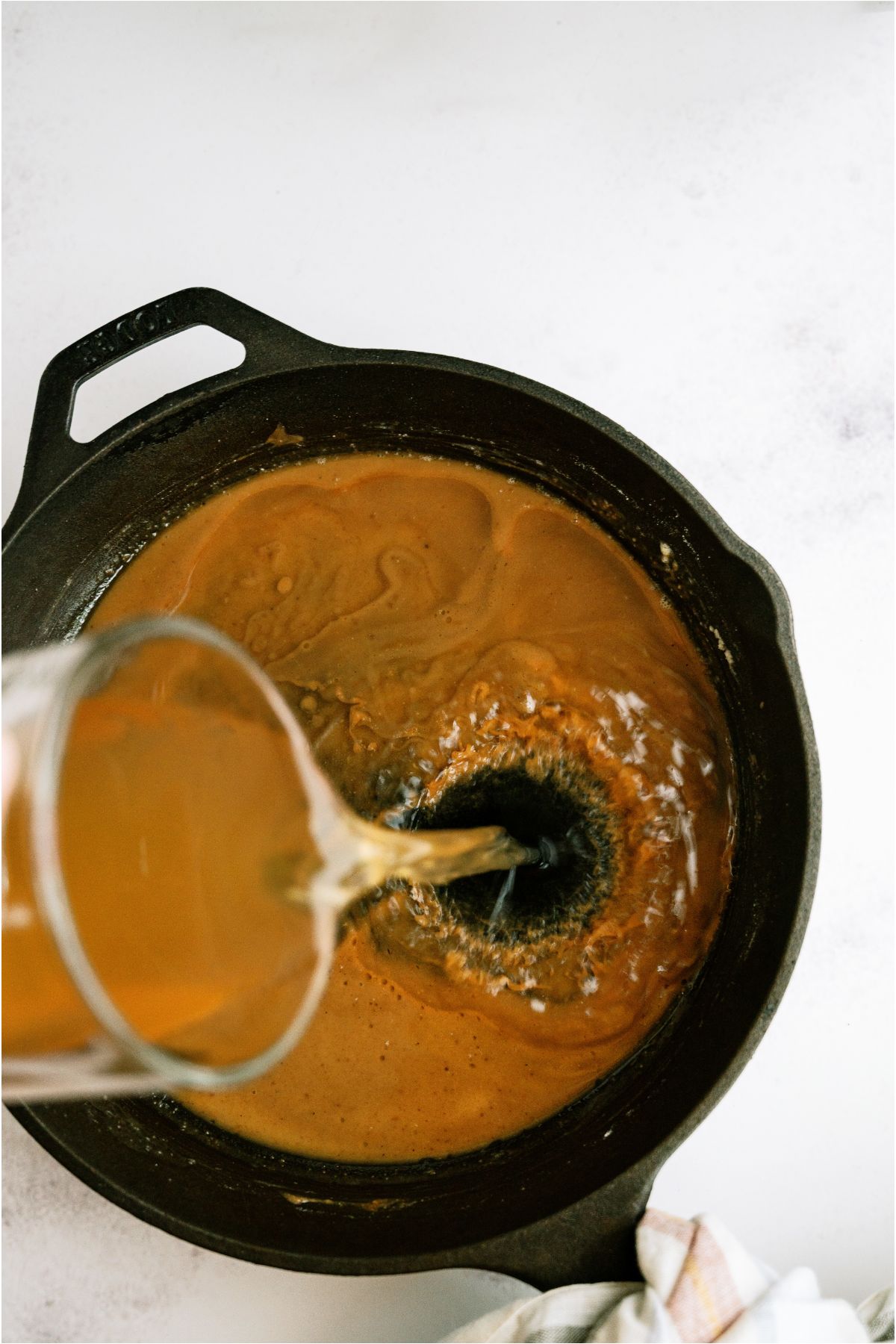 Pouring chicken broth into the skillet with flour to create a gravy.