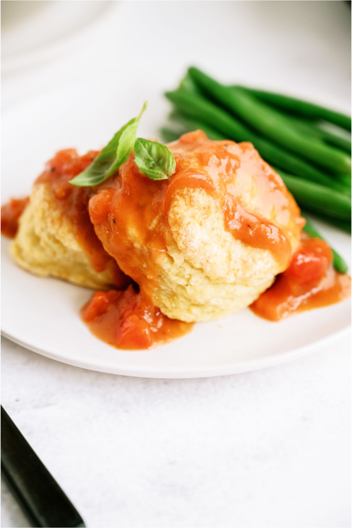 A white plate with two biscuits topped with Tomato Gravy (Traditional Southern Recipe) and green beans on the side.