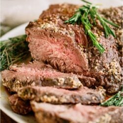 Garlic Butter Beef Roast on a serving plate with some if the roast sliced.