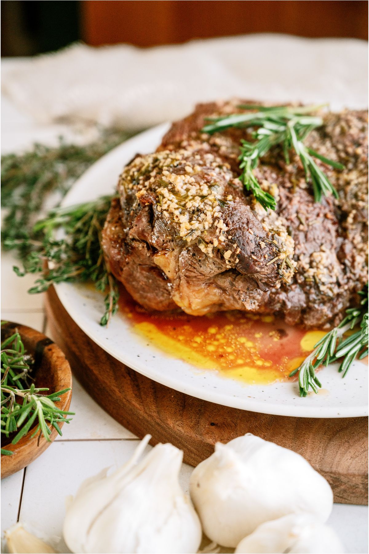 Garlic Butter Beef Roast on a serving platter with juices from the roast and fresh garlic in front of the platter.