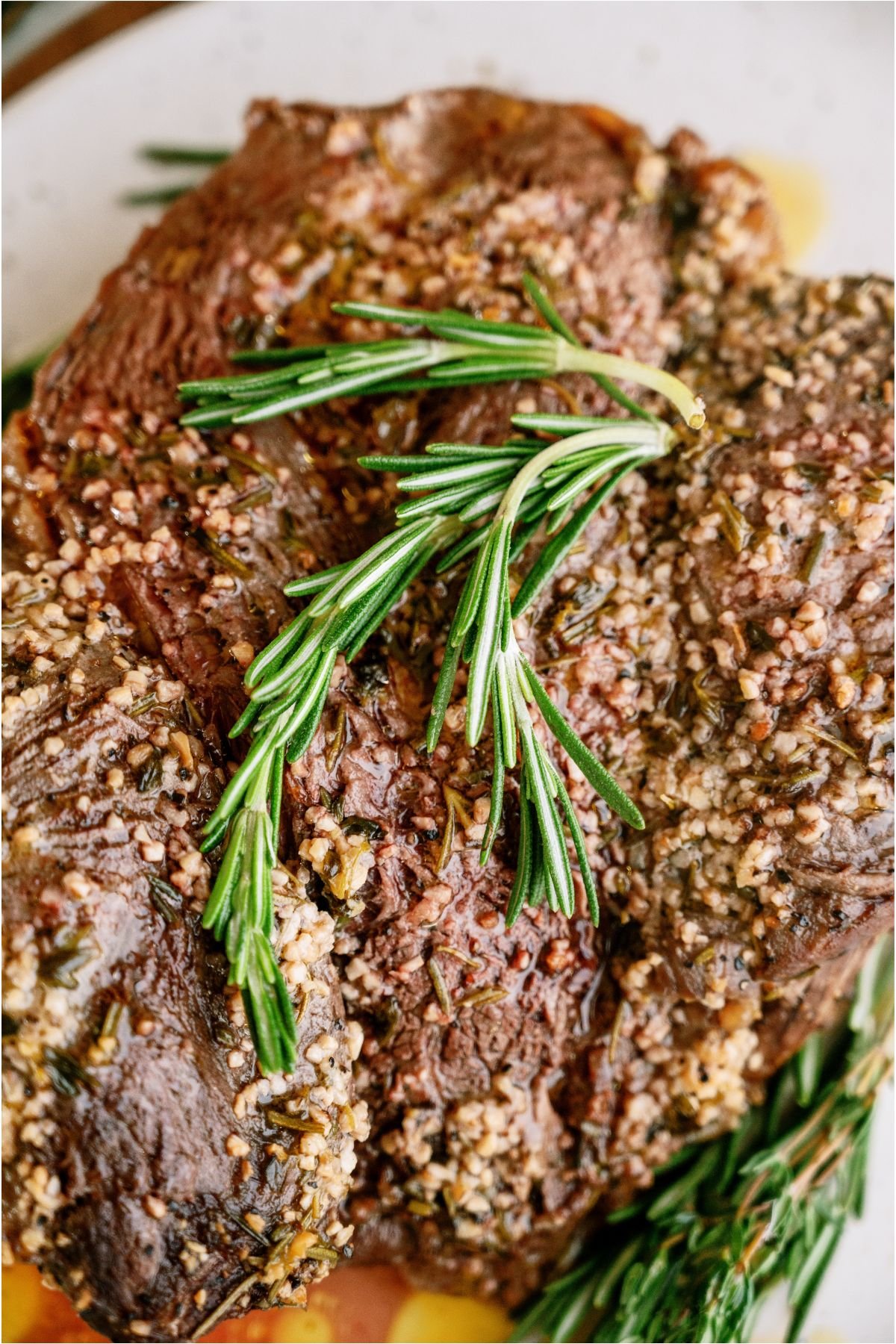 Top view of Garlic Butter Beef Roast with a sprig of  fresh rosemary on top of the roast.