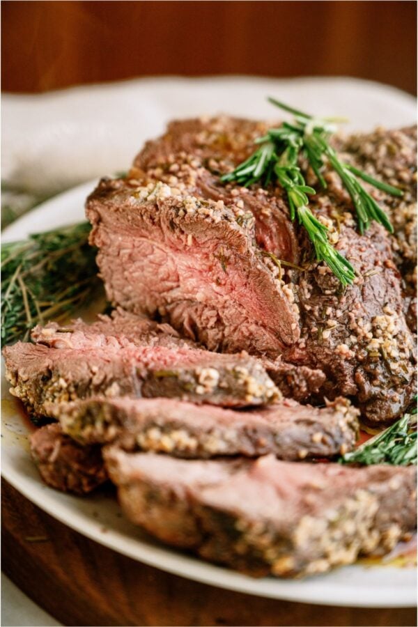 Garlic Butter Beef Roast on a serving plate with some if the roast sliced.