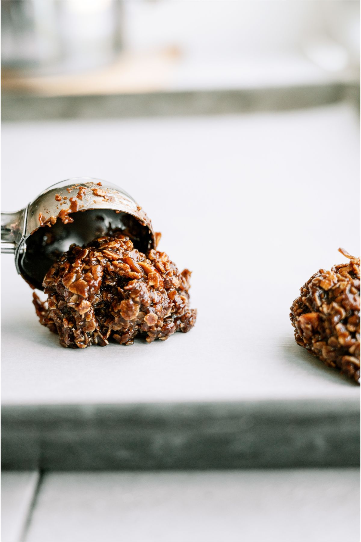 A scoop placing a ball of Haystack Cookie dough on a baking sheet lined with parchment paper.