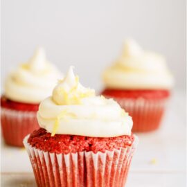 3 Red Velvet cupcakes with one in front and 2 in the background. Topped with frosting.