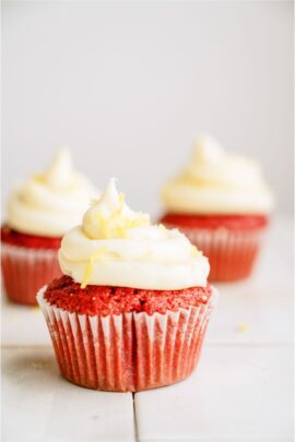 3 Red Velvet cupcakes with one in front and 2 in the background. Topped with frosting.