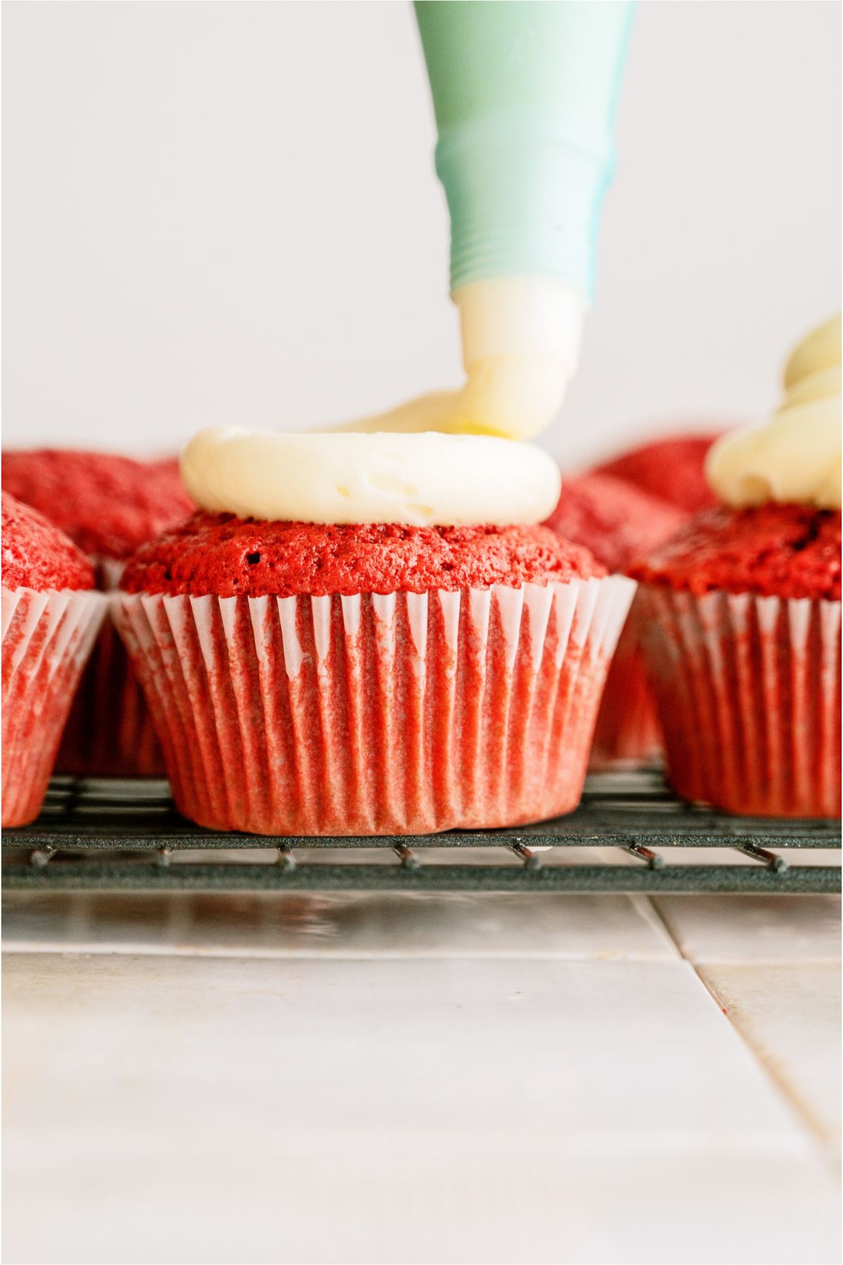 Piping frosting on top of Red Velvet Cupcake on a cooling rack.