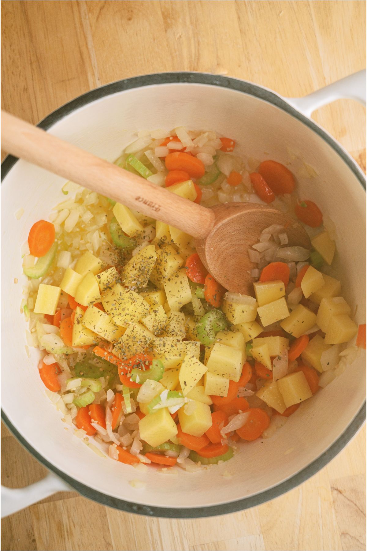 Chopped vegetables in a large saucepan sauteing with a wooden spoon. 