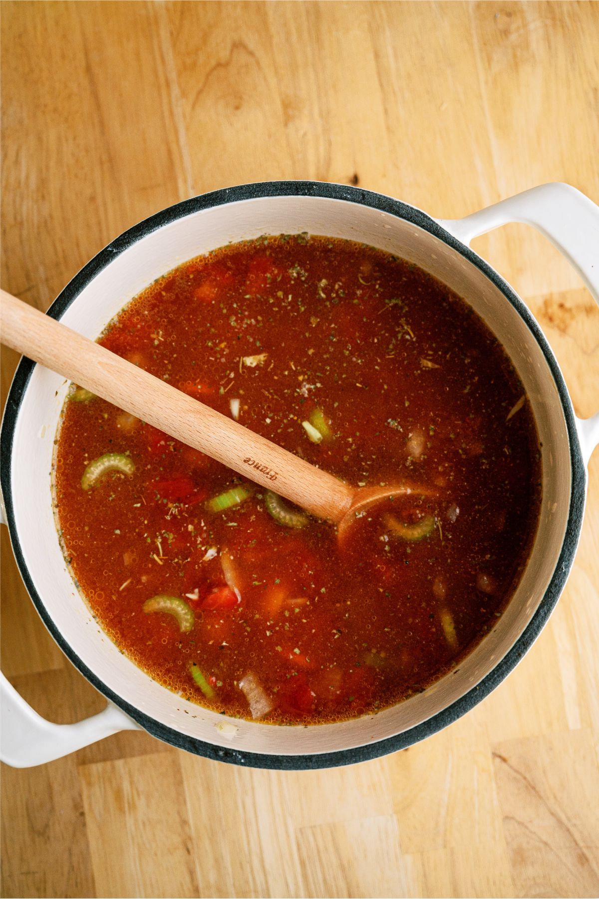 Vegetables, tomatoes and broth in a large saucepan with a wooden spoon.