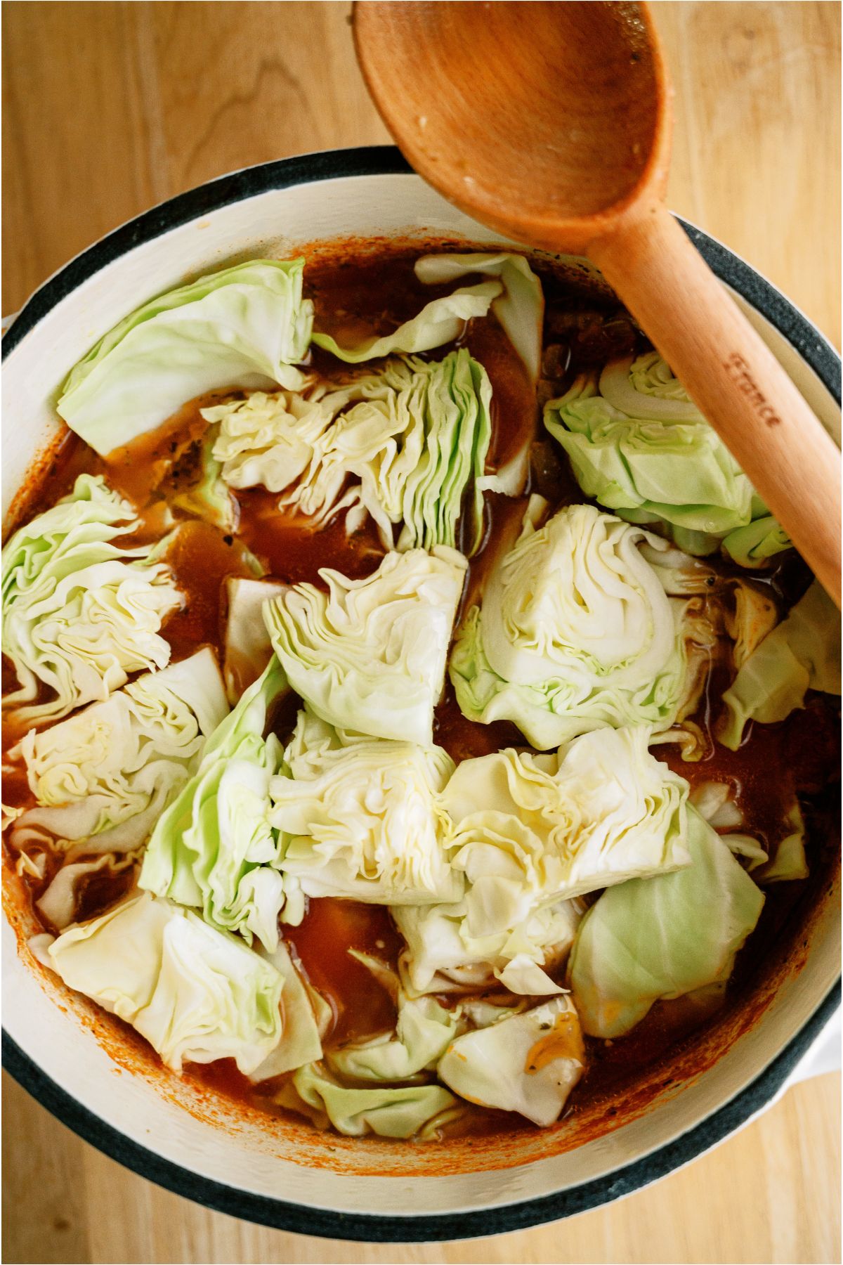 Large chunks of cabbage added to saucepan with vegetable broth mixture.