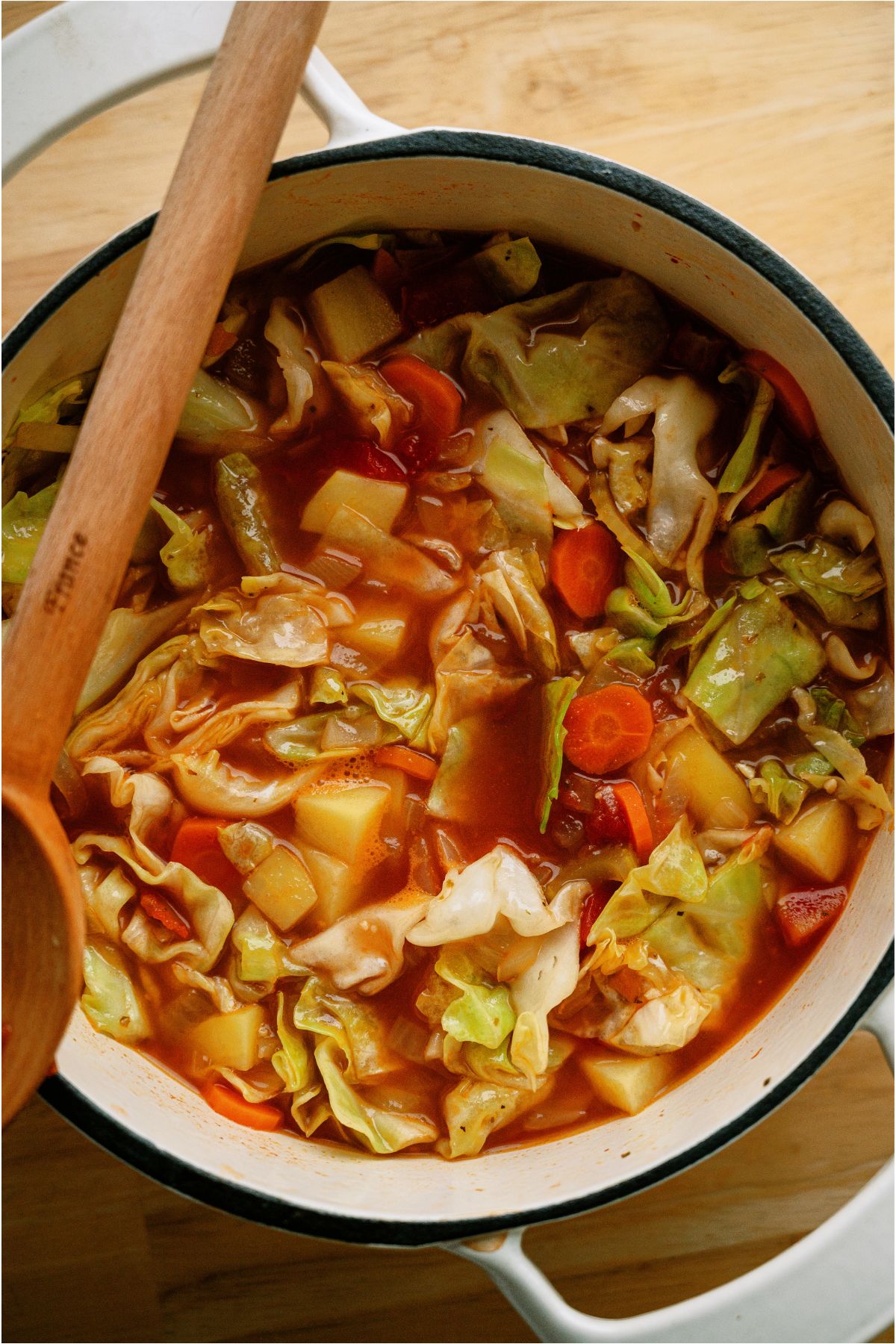 Cooked Cabbage Soup in a large saucepan with a wooden spoon.