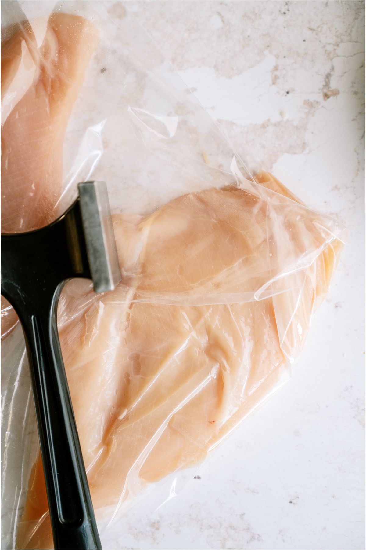 Raw chicken breasts in ziploc bags with a meat tenderizer.